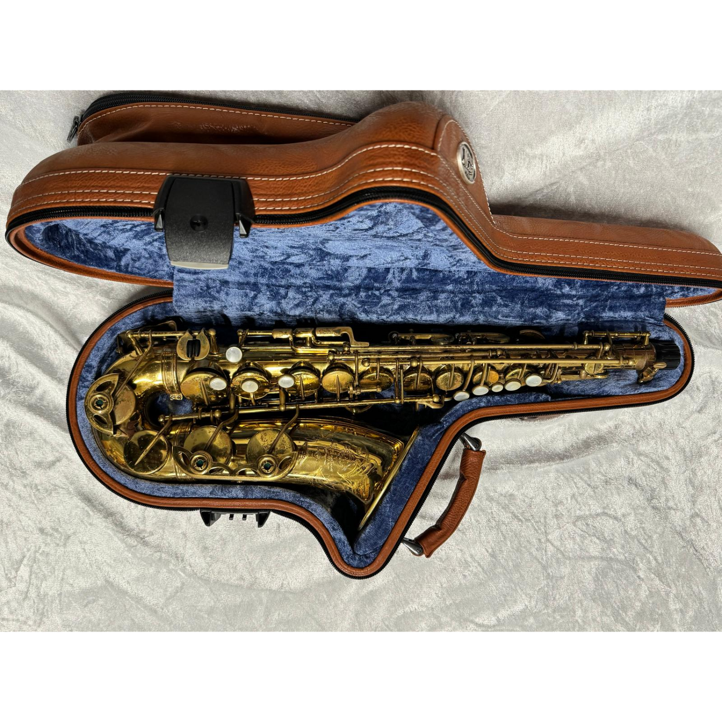 brown leather case laying open with saxophone inside on white velvet background