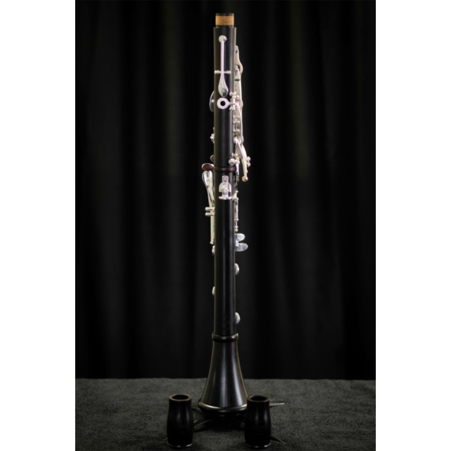 Rear view of Rossi Academy Bb clarinet on a stand, with 2 barrels sitting in front of it, against a black background