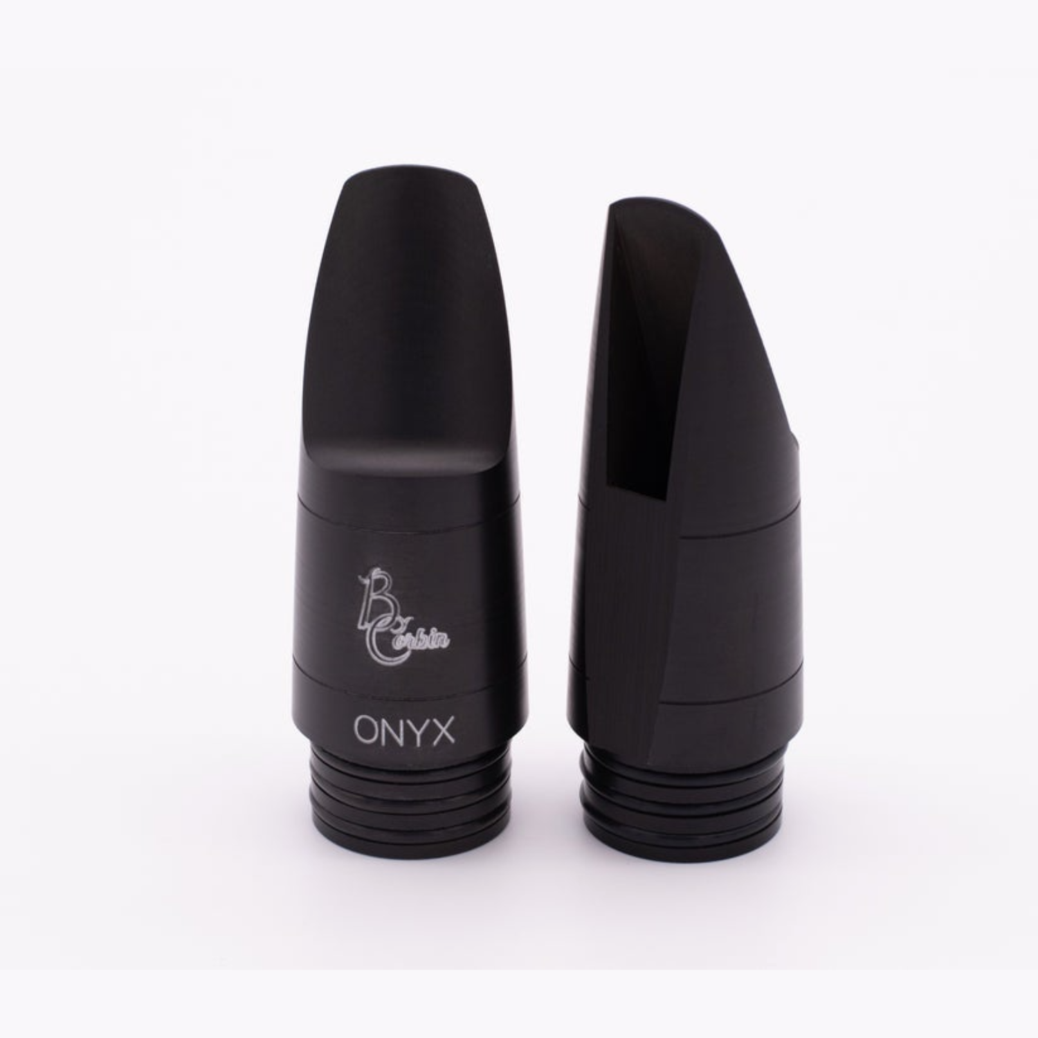 Two Corbin Onyx bass clarinet mouthpieces, one turned around to show the table and window, against a white background