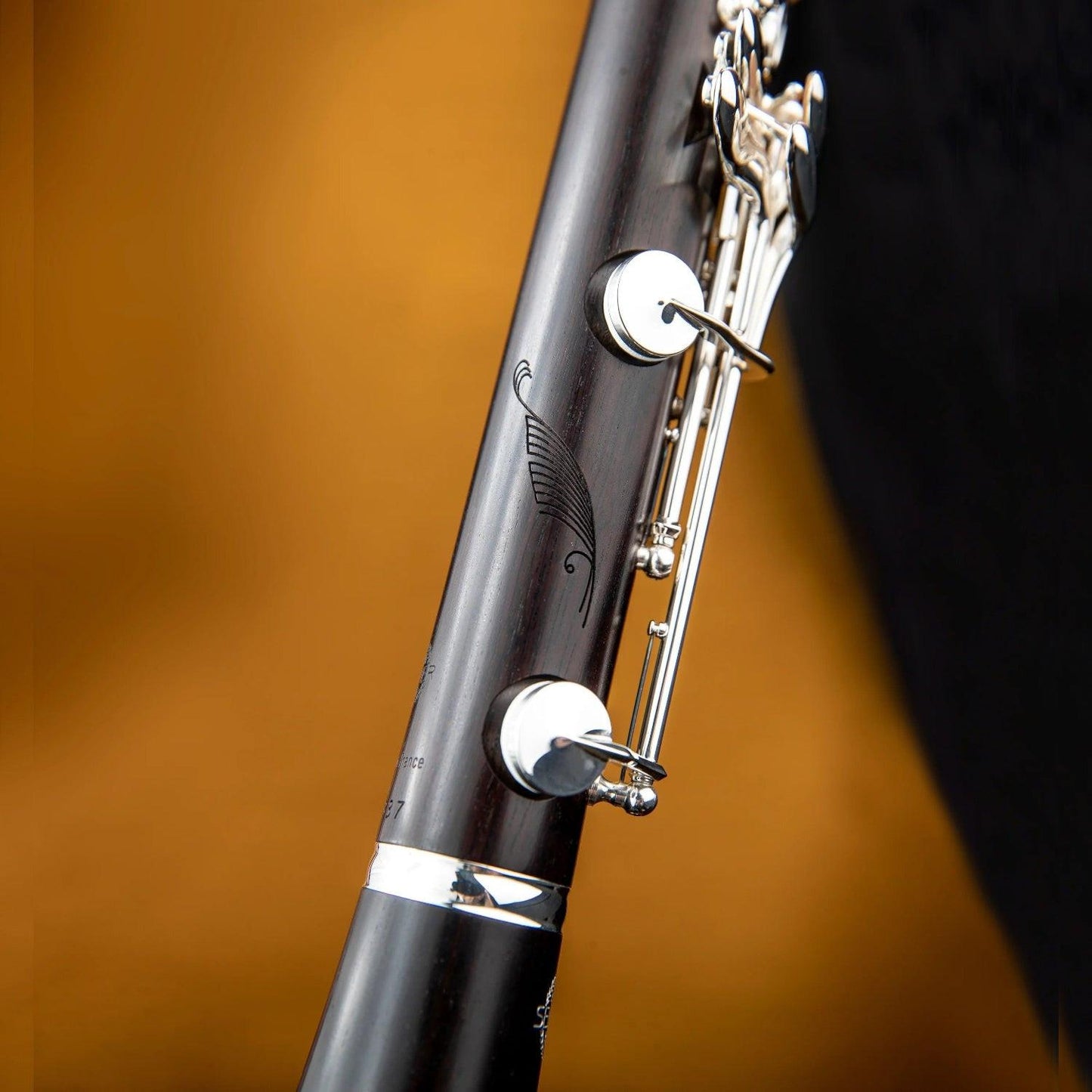 Closeup of the feather engraving in the wood on the side of the lower joint of the Selmer Muse clarinet, against a black and orange soft-focus background