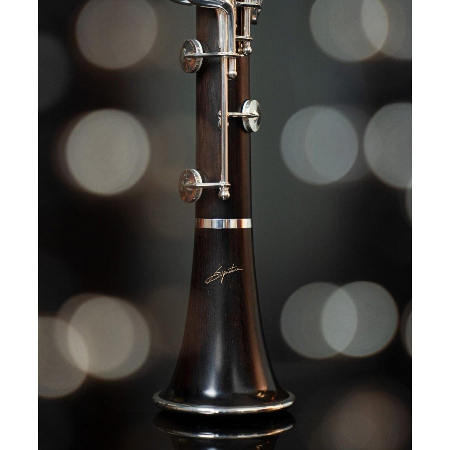 closeup of lower half of lower joint and bell, showing richly colored red-brown grenadilla wood and signature logo on the bell, against blurred bokeh background