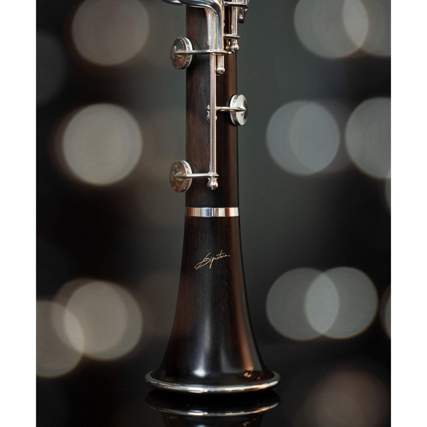 closeup of lower half of lower joint and bell, showing richly colored red-brown grenadilla wood and signature logo on the bell, against blurred bokeh background