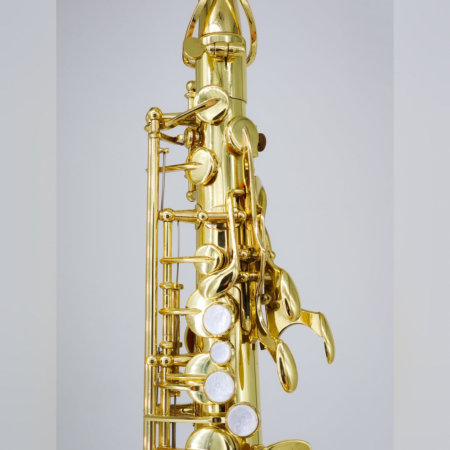 Close-up of a gold saxophone on a light gray background, focusing on front F key and palm keys