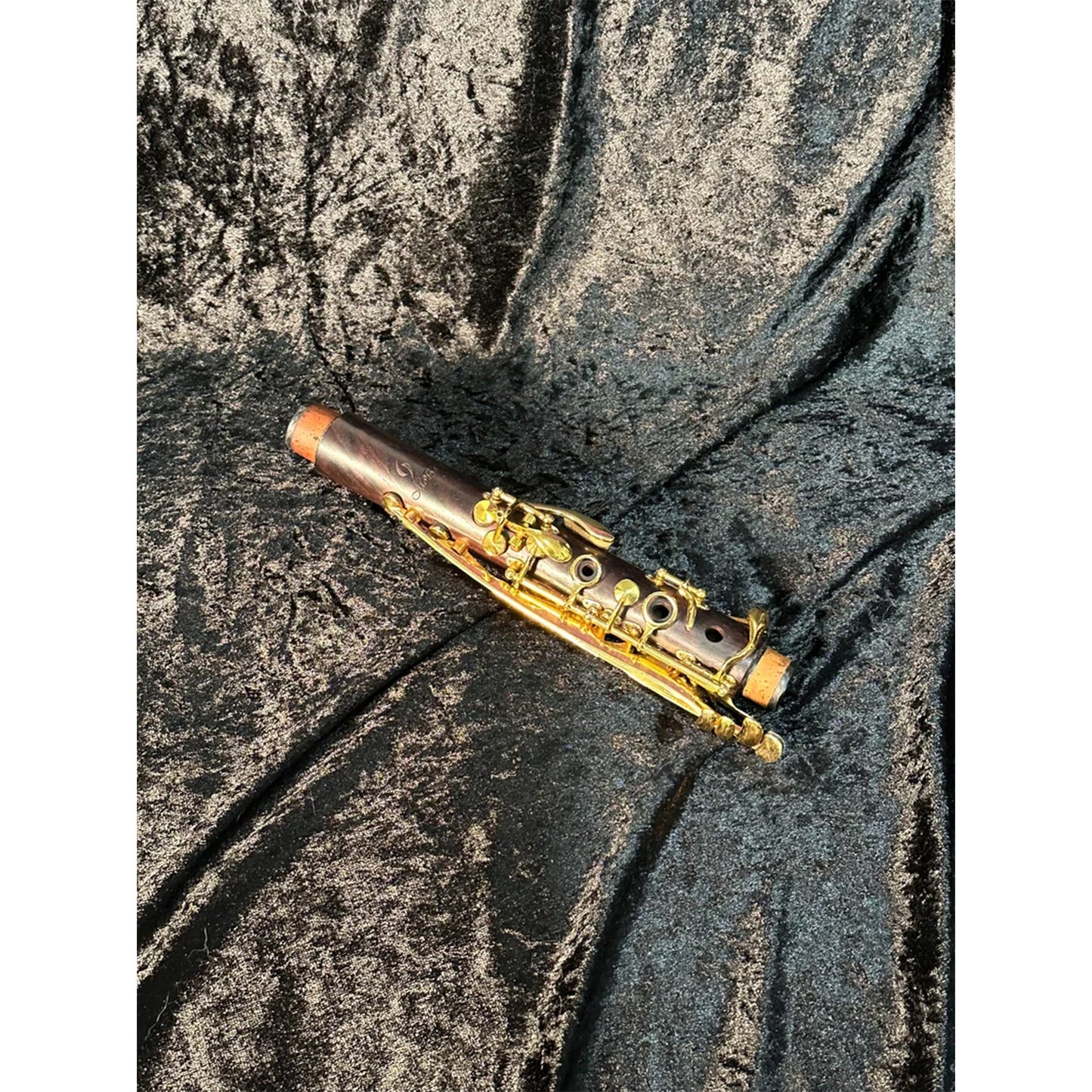 Upper joint of cocobolo Backun clarinet with gold keys, resting on black velvet background in bright light