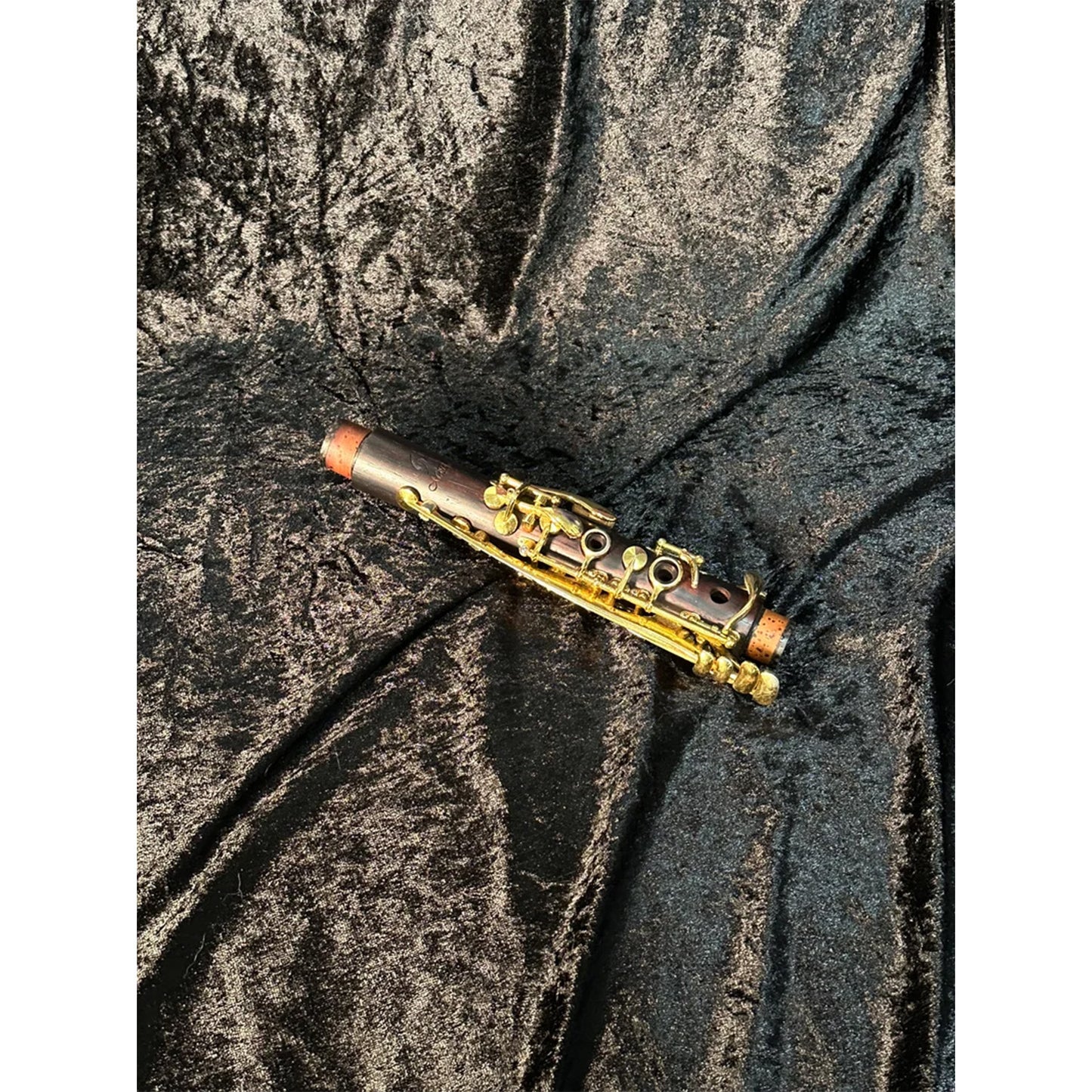 Upper joint of Backun cocobolo and gold Bb clarinet, on black velvet in bright light